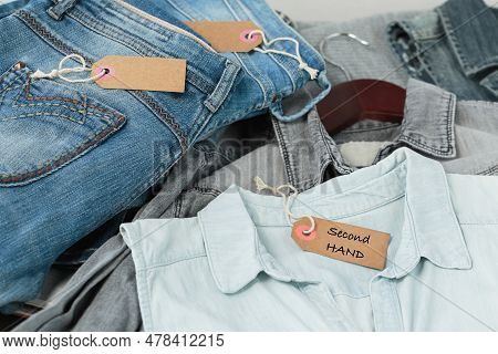 Stack Of Blue Jeans, Shirts And Tag With Inscription Second Hand. Second Hand Clothing Shop. Circula