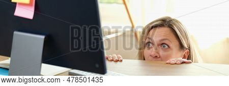 Portrait Of Surprised Woman Peeping Out Table And Looking At Pc Screen. Office Worker Hiding Under D