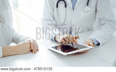 Doctor And Patient Sitting Near Each Other At The Desk In Clinic. The Focus Is On Female Physicians 