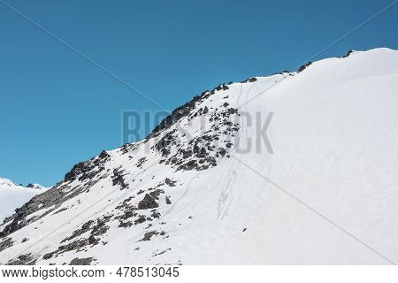 Climbers Footprints On Steep Snowy Slope Of High Snow Mountain With Rocks On Top. Snow-white Mountai