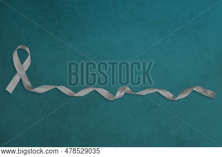 Photo Of Gray Ribbon With Curled End Atop A Blue-green Concrete Background.