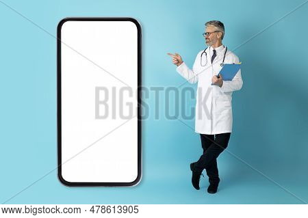 Positive Middle Aged Man Doctor Showing Huge Phone With Mockup