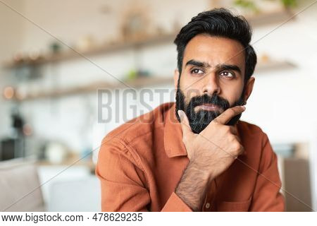 Portrait Of Pensive Young Arabic Man Thinking In Living Room