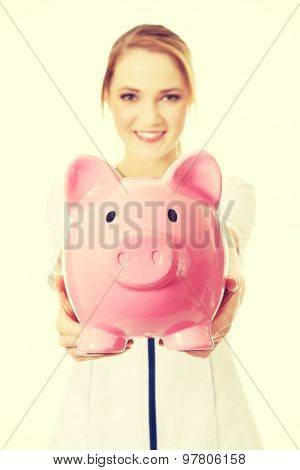 Young beautiful female doctor holding a piggybank.