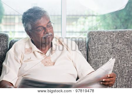 Senior Indian man reading newspaper at home. Asian old people living lifestyle indoors.