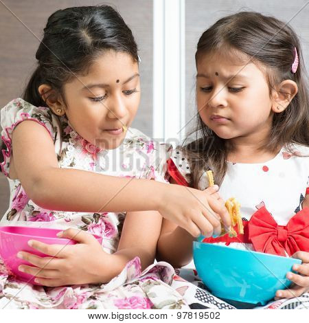 Indian girls sharing food, traditional snack murukku with each other. Asian sibling or children living lifestyle at home.