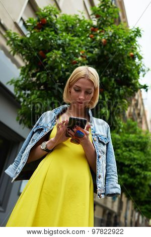Lovely young woman hold smartphone standing on beautiful mandarin trees background in city