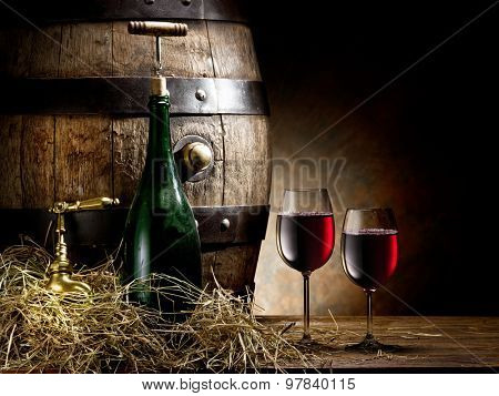 Still-life with glass of wine, bottle and barrel on the table in the cellar.