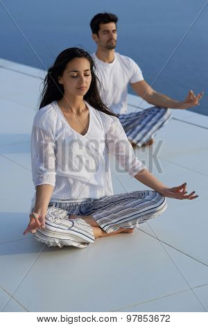 young couple practicing yoga at sunset in modern home terace with ocean and sunset in background