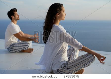 young couple practicing yoga at sunset in modern home terace with ocean and sunset in background
