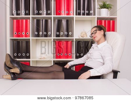 Portrait Of A Relaxed Young Businesswoman Sitting With Legs On Desk In A Bright Office