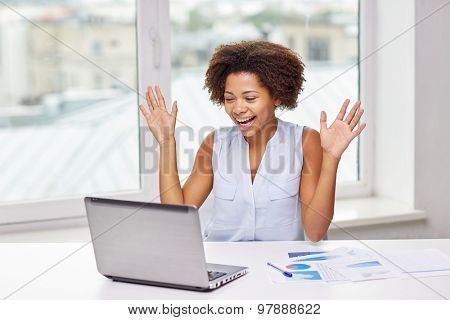 education, business, success and technology concept - happy african american businesswoman or student with laptop computer and papers at office