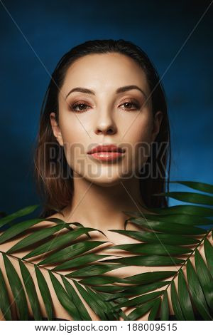 Vertical shot of amazing woman with wet slocked back hair. Covering shoulders with leaves.