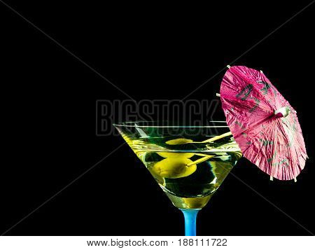 Cocktail glass with black background martini drink with olive and pink decotative umbrella