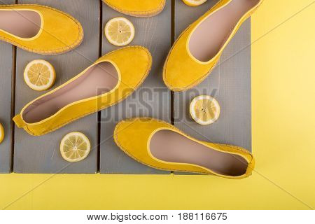 Yellow espadrilles shoes near slices of lemon on wooden background. Top view