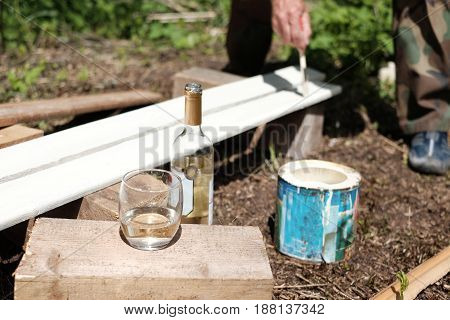 Bottle of wine and glass in the foreground and worker painting wood planks in the blurred background