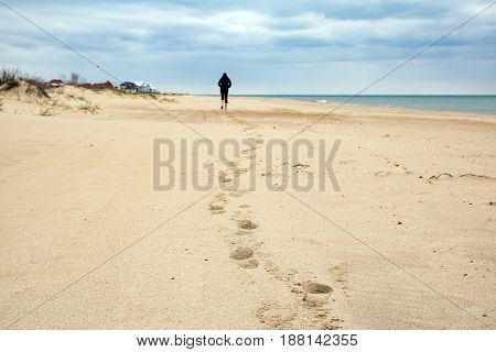 Woman Walks On The Beach To The Horizon Leaving Footprints In The Sand. Thunderclouds