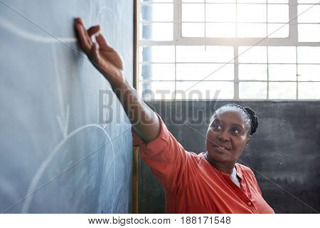 Focused young African businesswoman giving a blackboard presentation to unseen colleagues while standing in a modern office