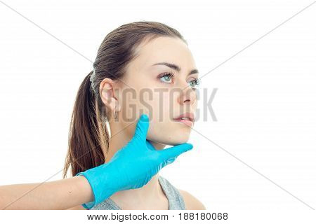 the face of a young cute girls at the beautician who keeps her face with his hand in a blue glove close-up isolated on background.