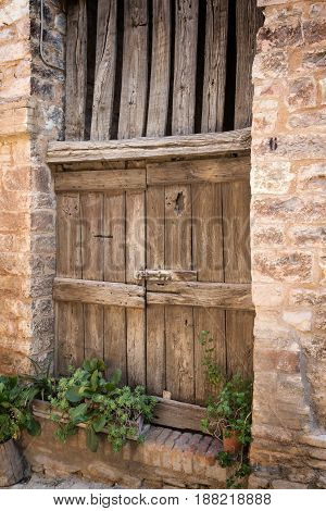 Side view of ancient wooden door in the old stone house decorated with plants in pots. Edited as a vintage photo.