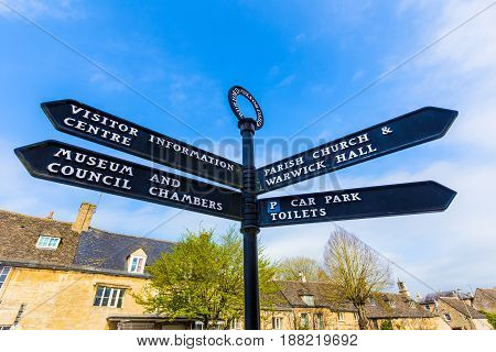 Burford Oxfordshire direction sign against blue sky and traditional Burford style buidling in background