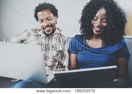 Front view of Happy african american couple relaxing together on the sofa.Young black man and his girlfriend using modern notebooks at home in the living room. Horizontal, blurred background
