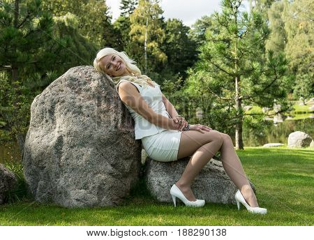 Blonde woman sitting on a stone. Young girl resting in nature natural environment background