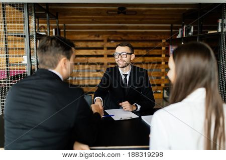 Sell Concept. Manager Greetings With  Couple At His Office.