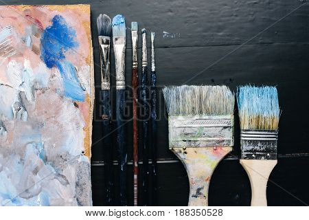 Artistic brushes and a palette lie on a black wooden table. Artist Tools