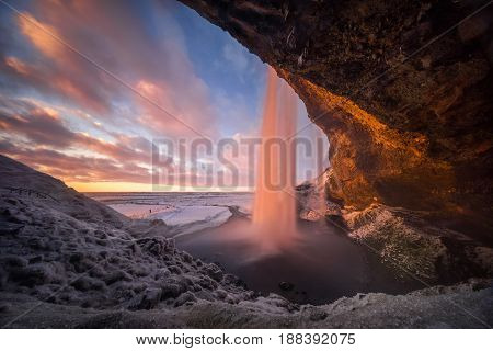 Colorful sunset in cave behind Seljalandsfoss waterfall in winter Iceland