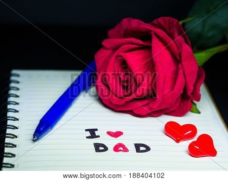 Father's day concept. I LOVE DAD message write on note book with red rose stack of books glasses and sweet marshmallow in the shape of heart on dark background