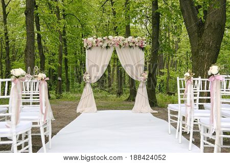 Beautiful wedding archway with lined up chairs with tenderless boutonnieres, outdoors