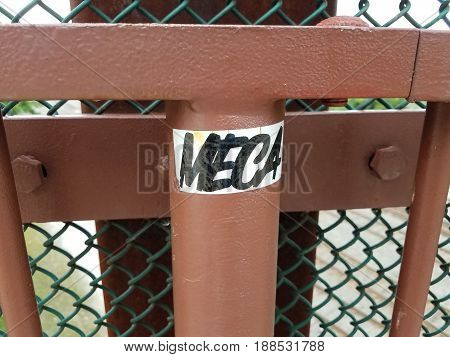 metal fence with holes and sticker saying meca on it