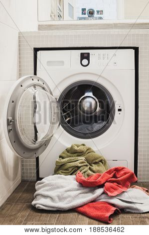Washing machine with multicolored dirty towels on the floor near it. laundry washer with opened door. Frontal view. Vertical