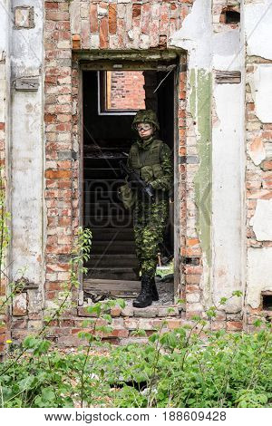 Portrait of armed woman with camouflage. Young female soldier observe with firearm. Child soldier with gun in war hearth house ruins background. Military army people concept