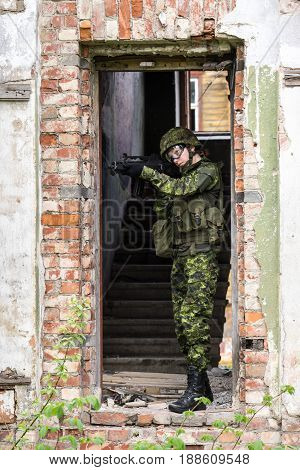Portrait of armed woman with camouflage. Young female soldier observe with firearm. Child soldier with gun in war hearth house ruins background. Military army people concept