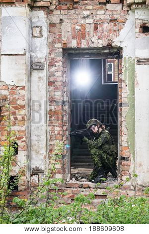 Portrait of armed woman with camouflage. Young female soldier observe with firearm. Child soldier with gun in war hearth house ruins background. Military army people concept