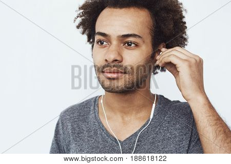Close up photo of young african man listening to music in headphones over white background.