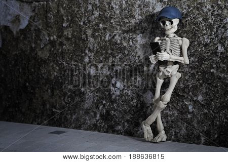 A skeleton leaning on a grungy wall with smartphone in his hand