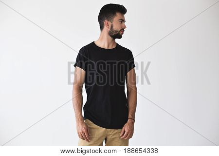 Handsome sporty strong man looks to the side posing in studio in blank simple black t-shirt and chinos shorts on isolated white mockup