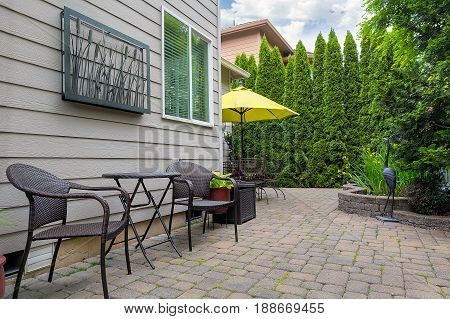 Bistro chairs and table on stone paver bricks patio in garden backyard with pond