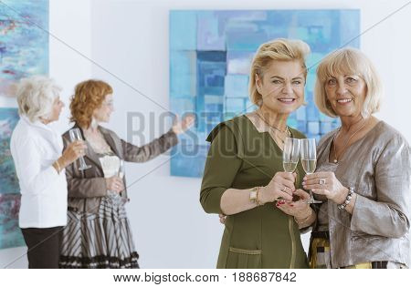 Four elegant women on opening in art gallery drinking champagne