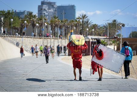 BARCELONA, SPAIN - MAY 2017: Beach lifeguard men are walking along the promenade of Barceloneta beach