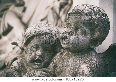 Little angels sculptures on a tomb at a graveyard. Toned image with selective focus.