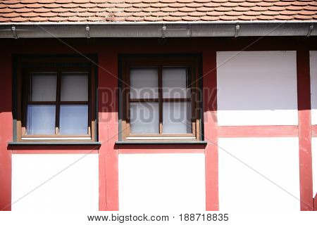 The close-up of the beam construction of a half-timbered house with windows in strong sunlight under the roof.