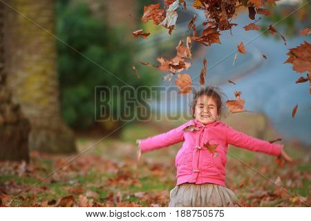 outdoor portrait of young happy child girl playing with autumn leaves in park on natural background