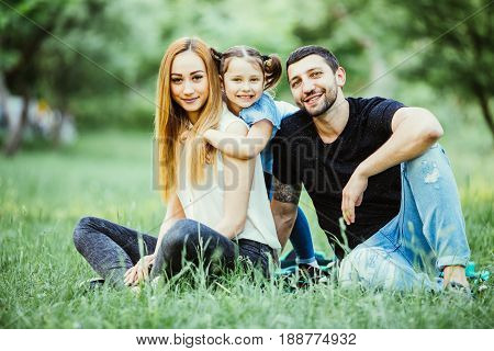 Young Happy Family In Summer Park. Father And Mother Spend Time In Summer Park With Their Daughter W