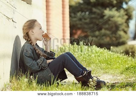 Poor little girl eating bread outdoors