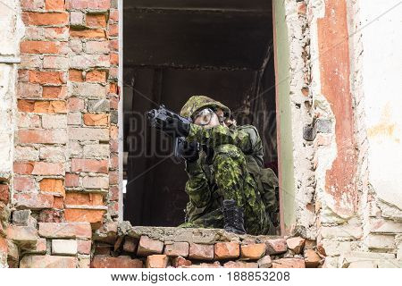 Portrait of armed woman with camouflage. Young female soldier observe with firearm. Child soldier with gun in war hearth house ruins background. Military army people concept