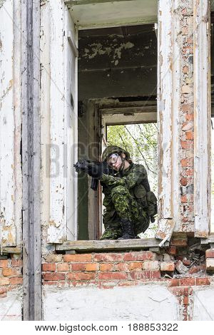 Portrait of armed woman with camouflage. Young female soldier observe with firearm. Child soldier with gun in war hearth house ruins background. Military army people concept